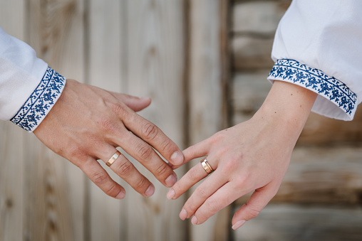 Rings and engagement. Bride and groom wearing embroidered dress and shirts hold hands together closeup. The Bride and groom holding hands. Hands are newlyweds with wedding rings.