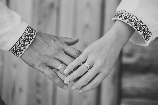 The Bride and groom holding hands. Hands are newlyweds with wedding rings. Rings and engagement. Bride and groom wearing embroidered dress and shirts hold hands together closeup. Black and white photo