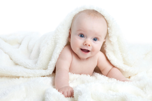 Baby girl lying on front, playing in white furry blanket isolated on white background.