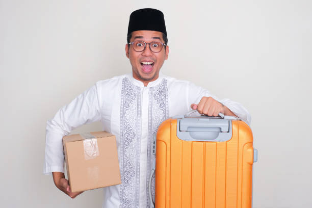 istock Moslem Asian man showing funny wow expression while carrying suitcase and package box 1872553509
