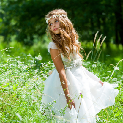 Cute girl holding white dress in green field.