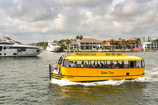 Fort Lauderdale, Florida, USA - 2 December 2023: Water taxi taking tourists past luxury houses and superyachts on one of the city's waterways