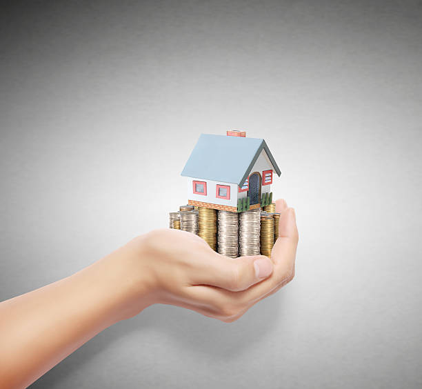 istock Hand holding different coins with a house resting on top 187257670