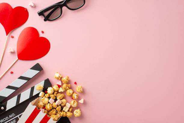 istock Valentine's film magic: top view clapperboard, 3D glasses, popcorn, heart decor, marshmallow, and sprinkles on a charming pastel pink setting. Capture the love in every frame 1872579885