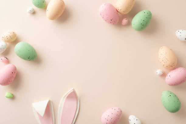 istock Easter magic in a single frame. Top view of lively eggs, bunny ears in focus, all on a pastel beige surface. There's ample space for your text or promotional content 1872579893
