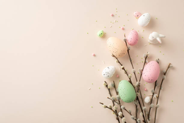 istock Celebration of Easter unfolds in this top-view composition. Traditional eggs, delicate pussy-willow branches, cute ceramic bunny, sprinkles adorn light beige surface with space for your text or advert 1872579904