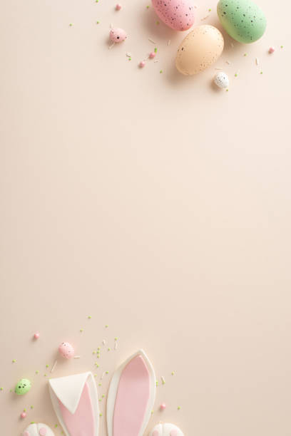Capture the essence of Easter in this composition. Vertical top view of festive eggs, cute bunny ears, and playful sugar sprinkles on a pastel beige backgroundâyour text or ad fits seamlessly