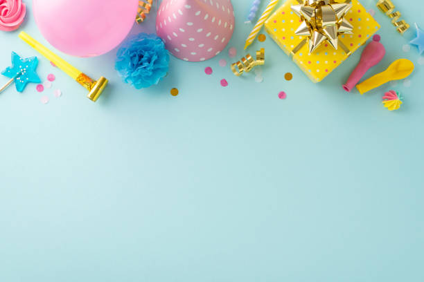istock Festive birthday bash idea. Top view of a table decked out with gift, birthday hat, pipe, candles, balloons, candies and confetti on a pastel blue surface. Ample space for text or promotions 1872579916
