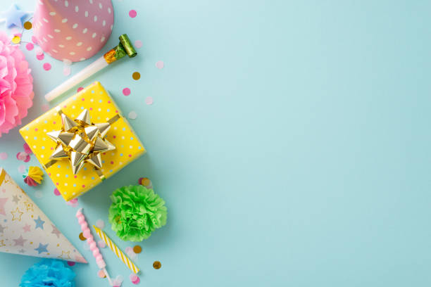 istock Festal gathering visualization. Top view shot capturing festive elements like candies, wrapped gift, birthday hats, party blower, candles, confetti on subtle sky blue background with space for text 1872579924