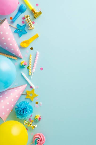 istock Animated celebration idea. Overhead vertical shot of a lively tabletop arrangement featuring sweets, party hats, pipe, candles, and balloons on a pastel blue setting. Adaptable for text or adverts 1872579933