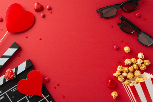 istock Top view romantic tableau featuring slate, 3D spectacles, popcorn box, delightful chocolates, sprinkles, heart-adorned sticks on vibrant red setting. Perfect for celebrating love and movie magic 1872580193