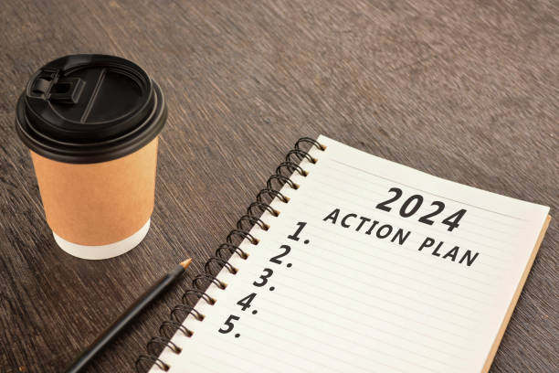 istock 2024 Action Plan text on Notepad with disposable coffee cup and pen on wooden desk. 1872610554