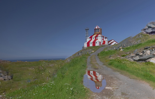 Bonavista Lighthouse is seen at the top of the hill, while it is partially reflecting in a pool of water at the bottom of the hill.