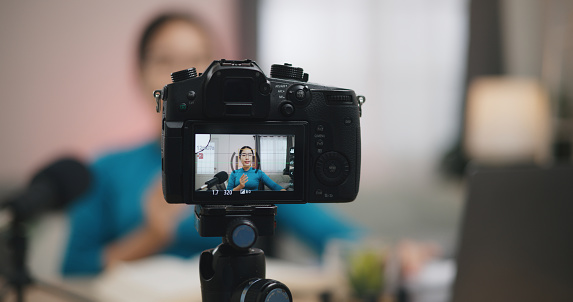 selective focus on digital camera while young asian woman in glasses talking on microphone to recording video tutorial for Internet. side hustle occupation at home concept.
