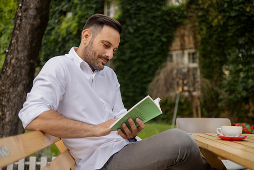 Bearded Mid Adult Man Reading Book While Sitting in Outdoor Cafe