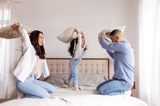 pillow fight, little Asian girl plays with her parents on the bed at home, Korean parents spend time with their daughter and rejoice, mom and dad have fun with the child