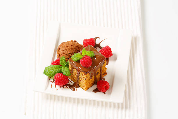piece of gingerbread cake with chocolate, chocolate ice cream and fresh rasberries on white square plate