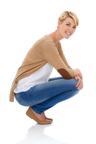 A pretty young woman crouching in casual wear while isolated on a white background