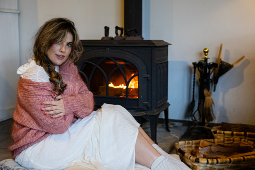 Portrait of woman sitting in front of the fireplace relaxing in comfortable clothes looking at the camera relaxing and resting