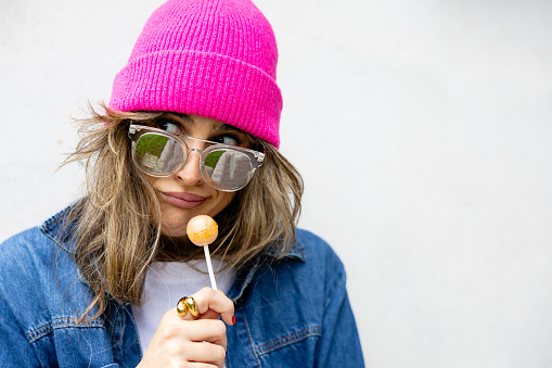 Portrait of girl with cap and sunglasses with a lollipop with funny expression, white space