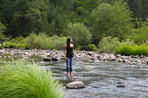 Beautiful young hispanic woman standing in mountain river.