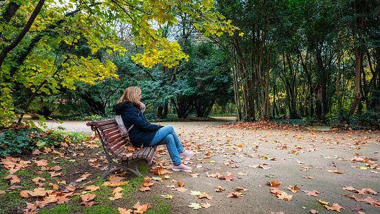 Woman sitting on a wooden bench in public park on a cold winter day
