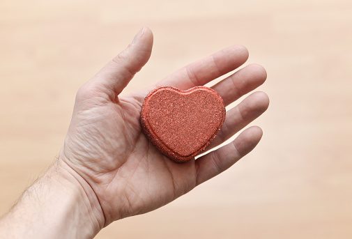 Closeup of a man's hand holding a heart shaped box symbolizing a Valentine's Day gift.