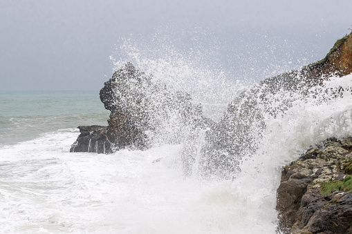 Waves breaking over rocks on gray day