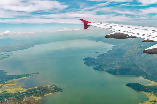 View from the window of an airplane on the wing against the backdrop of a sea bay among the mountains. Aerial view through glass of a beautiful landscape. Flight over the Balkans