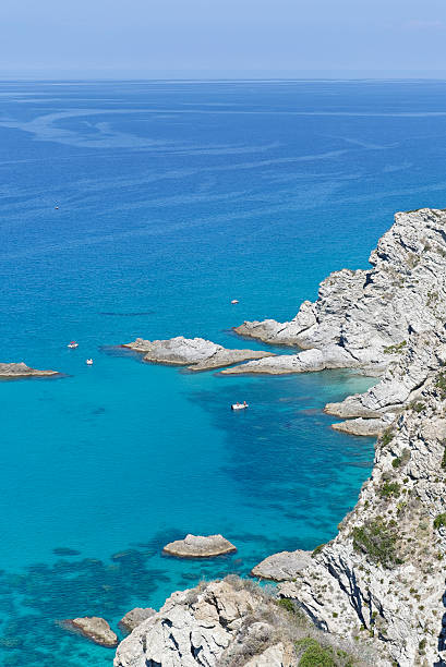 Crystal clear azure water and rock formations at Capo Vaticano, located  in the commune of Ricadi in Calabria, Italy. Some pedalos and a motor boat along the coast. 