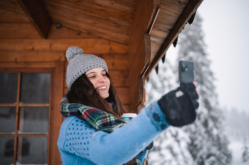 Woman on a winter vacation taking a photo of view next to mountain hut.