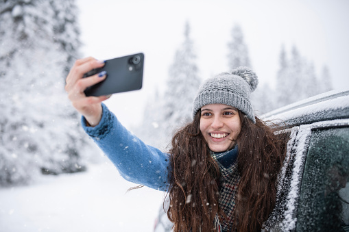 Young woman in a car in the winter taking a selfie with her phone.
