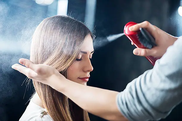 Hairdresser spraying his customer's hair.