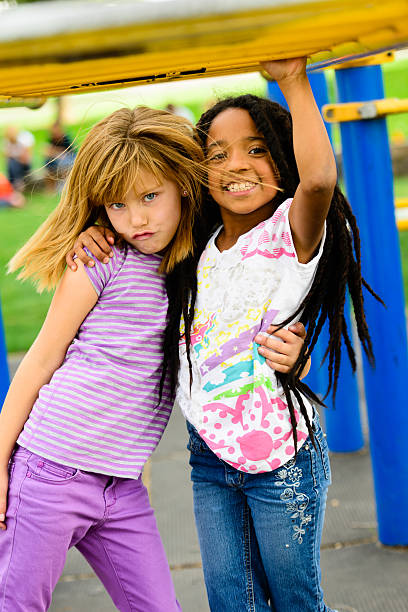 An African-American and Caucasian girl playing together under the monkey bars, playground.  Could be sisters or friends.