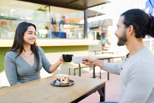 Happy attractive couple in their 20s smiling having a romantic date at the outdoor cafe and drinking coffee with dessert