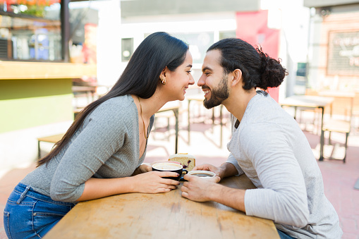 Profile of an attractive happy hispanic couple about to kiss and smiling while having a coffee date at the outdoor cafe