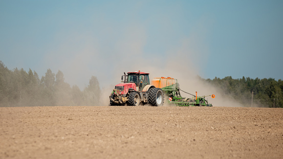 A powerful farm tractor with a mechanical plow raises dust on a hot day - machinery cultivates a farm field