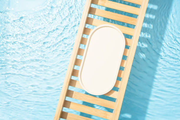 Cosmetic product presentation flat lay scene made with empty tray on bath tray above the transparent blue water. Template for self-care product placement.