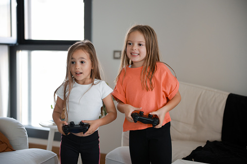 Two happy girls sitting on sofa and playing video game at home.