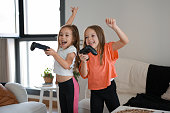 Two sisters kids playing video games at home together. Happy childeren, carefree childhood concept