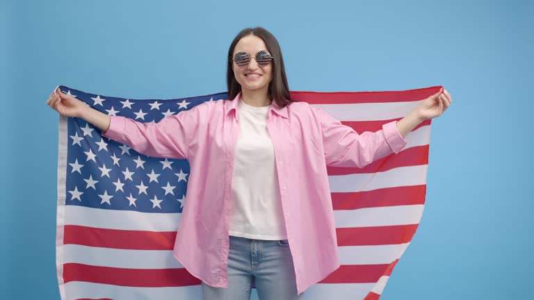 Happy smilling girl in american glasses waving and wrapping in American USA flag, celebrating, human rights and freedoms. Independence day