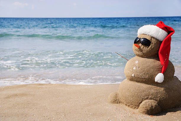 boneco de neve areia no chapéu do pai natal.  conceito de férias de natal - christmas beach sun tropical climate imagens e fotografias de stock