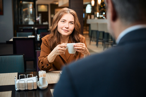 Cropped photo of elegant lady holding cup in hands while sitting in cafe