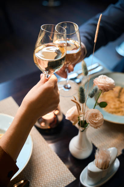 imagen parcial de una pareja brindando por el vino de las copas en la mesa en el restaurante del hotel - hotel restaurant women luxury fotografías e imágenes de stock