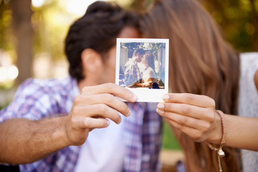 Shot of a young couple holding up a polaroid picture in front of them while sharing a tender moment