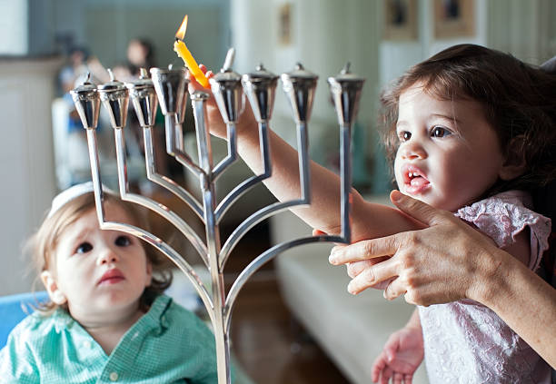 Young girl lights the Hanukkah menorah with help from adult Lighting the Hanukkah Menorah yarmulke photos stock pictures, royalty-free photos & images
