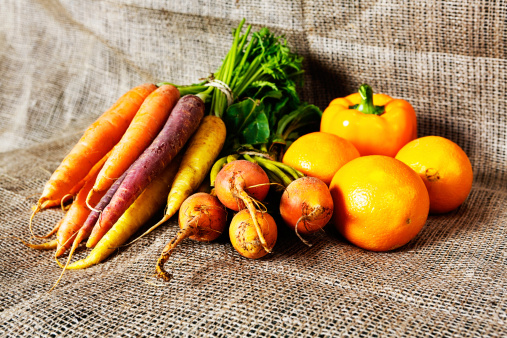 Heirloom carrots, citrus, turnips and yellow peppers make a glowing golden group of vegetables on burlap.