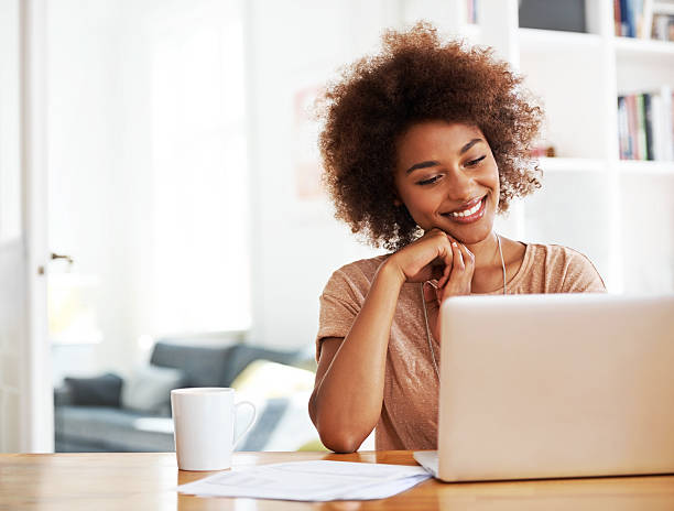 A beautiful African- american woman sitting at a table and looking at her laptop with a cup of tea beside her