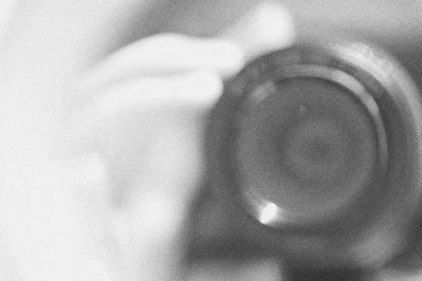 Photo of a woman with an old bellows camera. She holds the camera in front of her face and presses the shutter release.