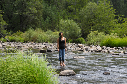 Beautiful young hispanic woman standing in mountain river.